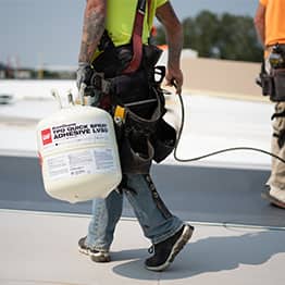 a roofer carrying a canister of tpo quick spray adhesive