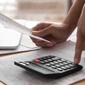 Human hand with calculator and paper reviewing credit card information.