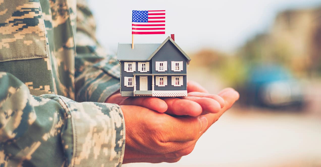 US military officer holding a doll house with flag, symbolizing GAF roofing rebate for troops.