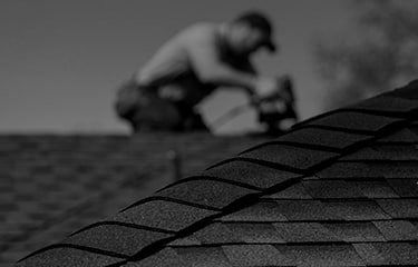 Shaded image of a GAF roofer installing GAF hip and ridge cap shingles to a residential roof