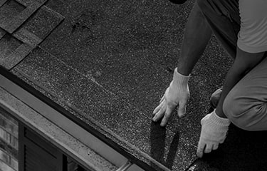 Shaded image of a roofer with white gloves installing GAF starter strip shingles to prevent shingle blow-off