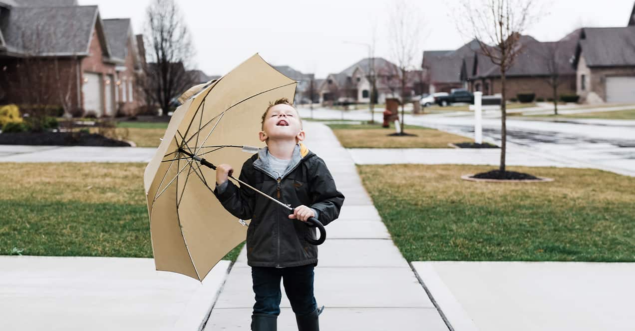 child holding an umbrella catching raindrops outside in rainy neighborhood