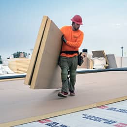 GAF contractor carrying insulation panels on a commercial roof job site
