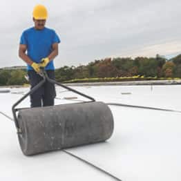 roofer rolling pvc membrane over a roof deck