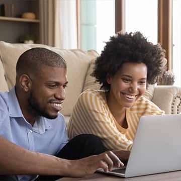 Man and women smiling while reviewing items on a laptop.